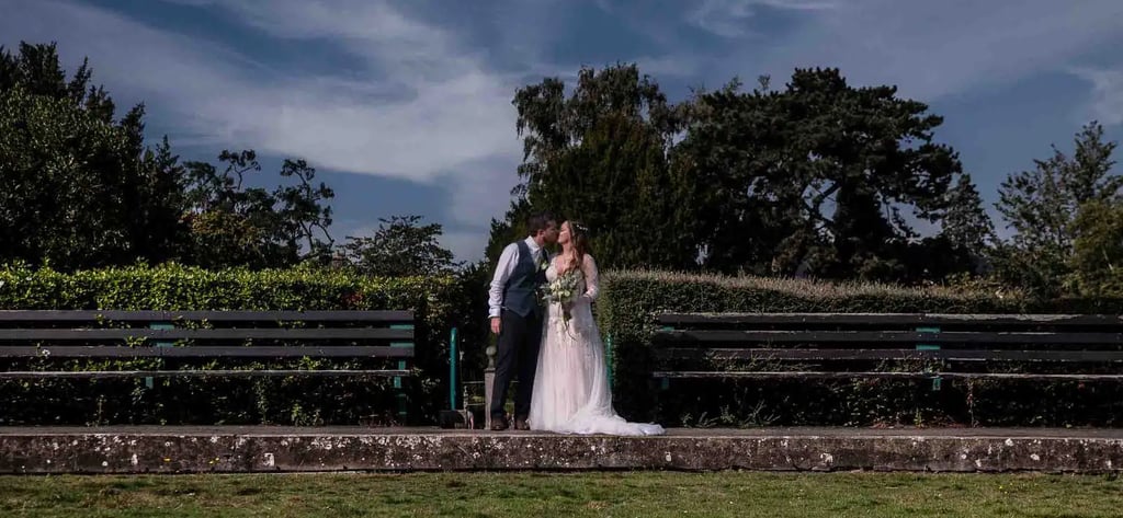 a bride and groom kissing on a bench in a park