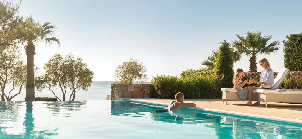 A family relaxing by a luxury infinity pool at a tropical oceanfront resort.