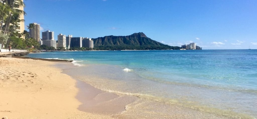 Vista da praia de Waikiki com mar calmo e a cidade de Honolulu ao fundo