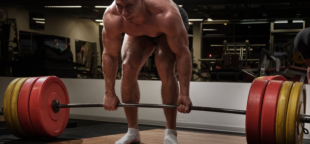 Muscular bodybuilder performing a heavy barbell deadlift exercise on a platform in a gym.