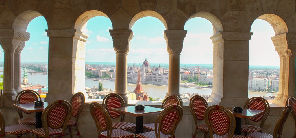 veduta del parlamento di budapest attraverso una terrazza con tavolini e protetta da piccoli archi 