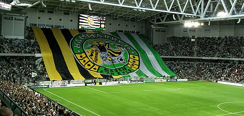 Blick auf die Spielfläche und die vollbesetzten Tribünen der Tele2 Arena, Heimstadion von Hammarby IF, mit Fans, Fahnen und F