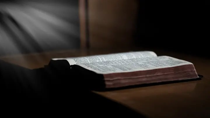  Bíblia aberta sobre mesa com feixe de luz iluminando suas páginas.