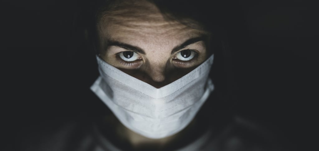 Individual with a white face mask and visible eyes against a dark background, highlighting awareness