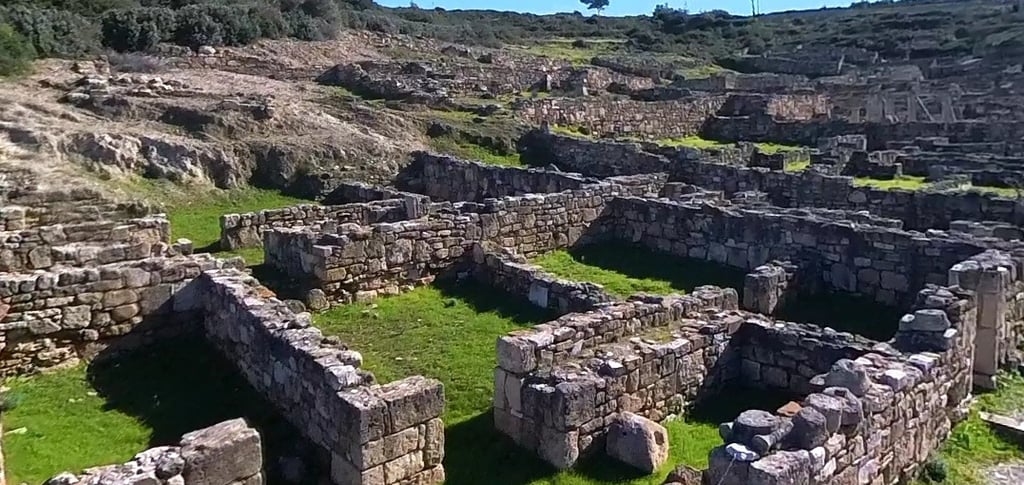 Ancient stone ruins of the city of Kamiros on Rhodes island with green grass under a clear blue sky.