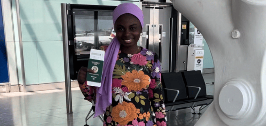 A Nigerian girl wearing a colourful dress, holding a Nigerian passport in an airport in London