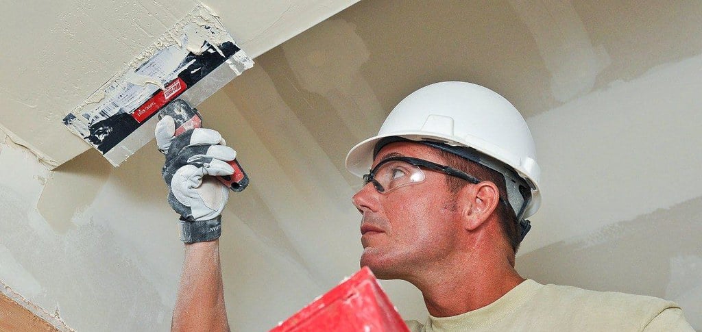 man using drywall knife to apply mud