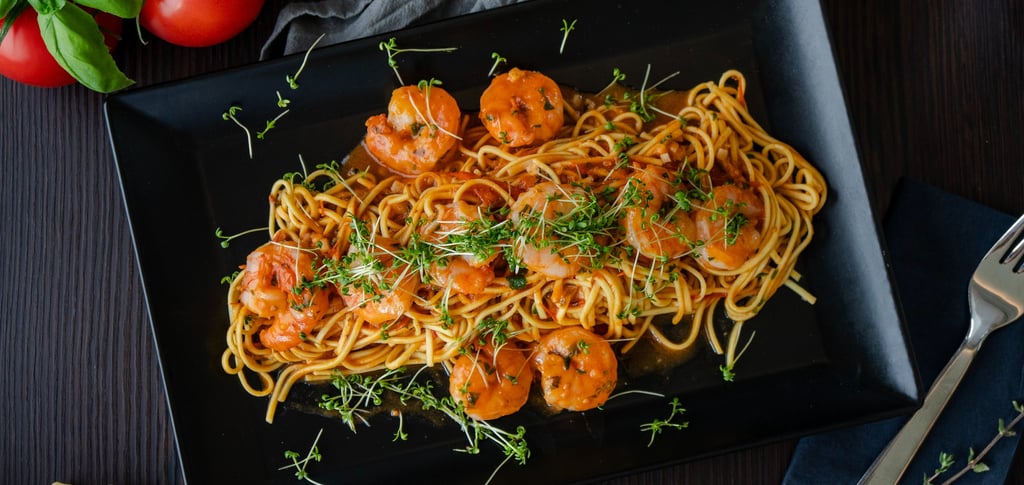 Gourmet Shrimp Pasta mit Tomatensauce und Microgreens auf schwarzem Teller