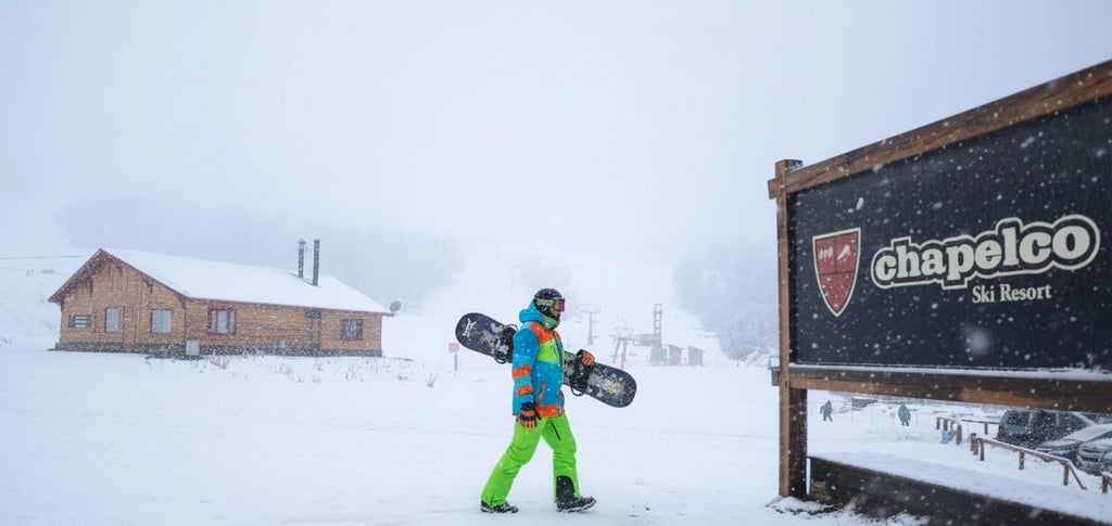 a man in a bright green jacket and green pants holding a snowboard chapelco argentina