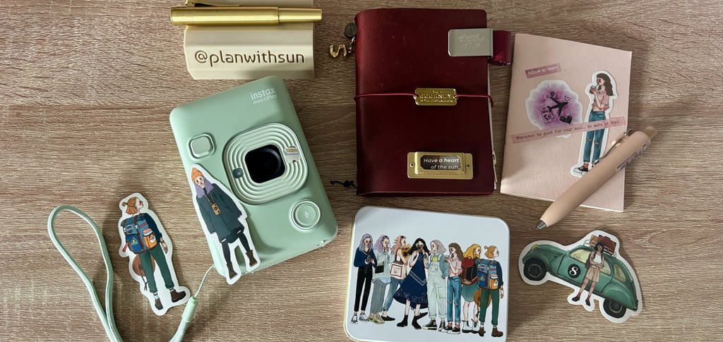 Flat lay of an Instax Mini LiPlay camera, leather journal, and journaling stickers on a wooden desk.