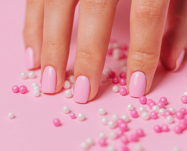 a hand with pink nail paint and some pearls