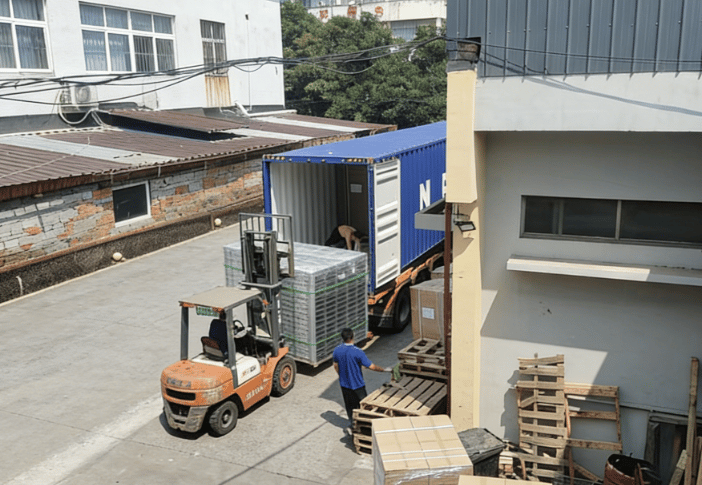 Forklift loading palletized boxes into a blue shipping container at an industrial warehouse dock.