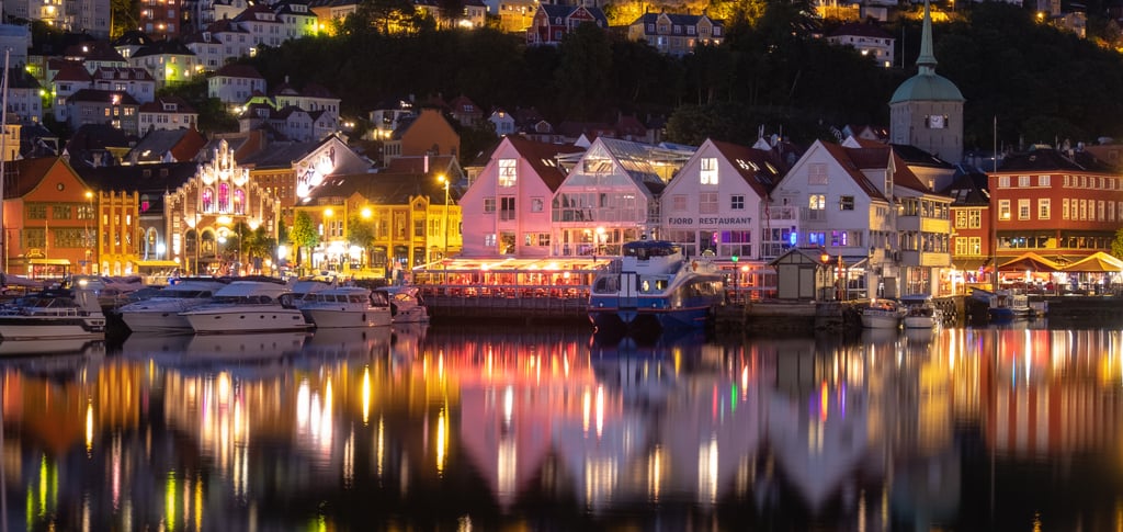 Night view of Bergen, Norway's historic harbor with illuminated waterfront buildings and colorful reflections.