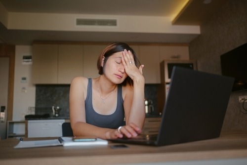 Stressed woman rubbing her eyes while working on a laptop at home to relieve digital eye strain.