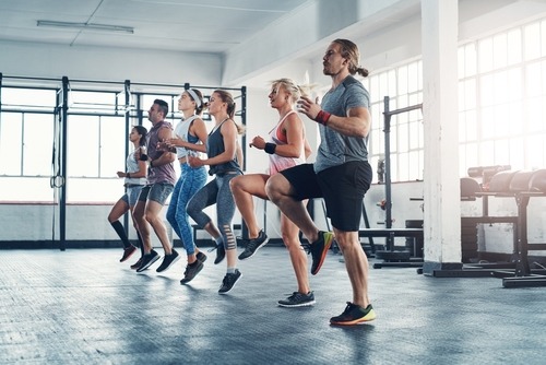 A diverse group of people doing high knee cardio exercises during a group fitness class in a gym.