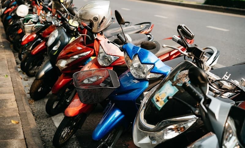 Eine Reihe bunter Motorräder und Roller parkte entlang des Bürgersteigs einer Stadtstraße.