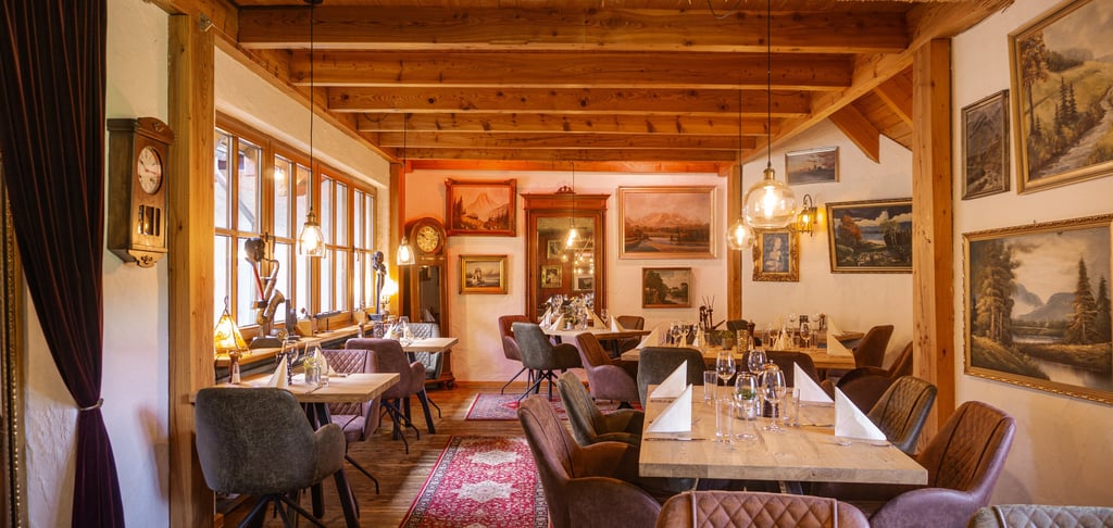 Rustikales Fine-Dining-Restaurant mit Holzbalken, Kunstwerken und eleganter Tischgestaltung.