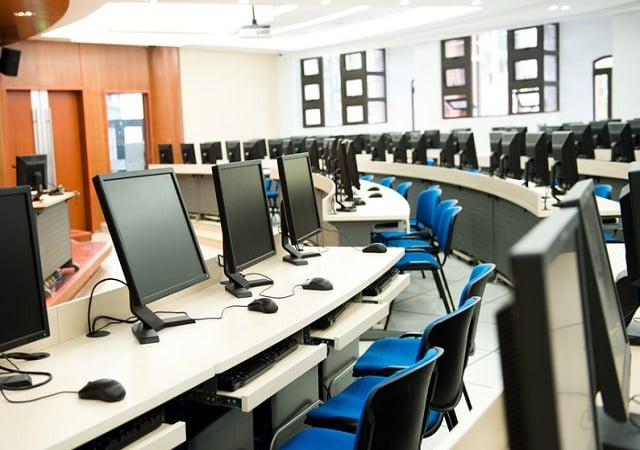 Modern university computer lab featuring rows of monitors and blue chairs for student learning.