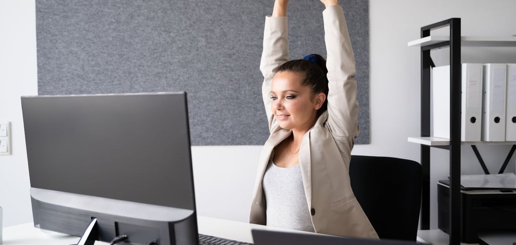 a woman sitting at a desk with her arms up in the air stretching