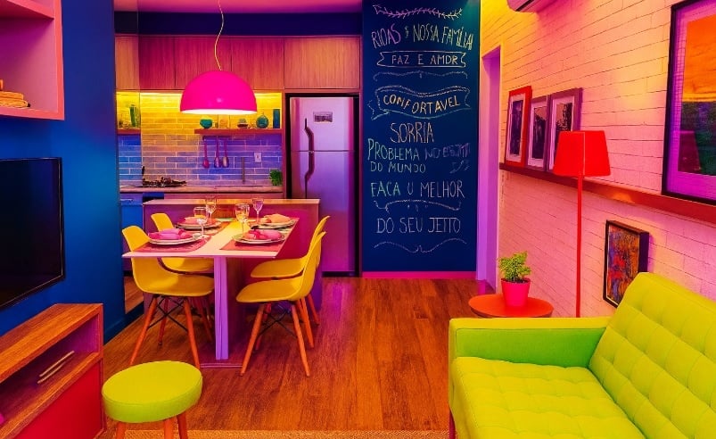 Apartamento alugado com decoração vibrante: sala integrada à cozinha com sofá verde-limão, cadeiras