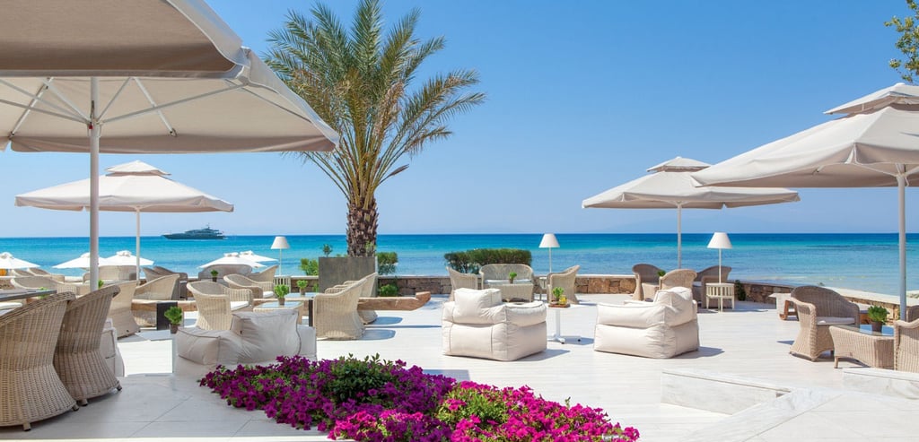 Luxury beach club Sani  white lounge seating, patio umbrellas, and palm trees overlooking the ocean.
