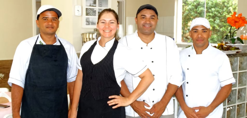 A smiling restaurant kitchen staff and servers posing in professional uniforms and chef hats.