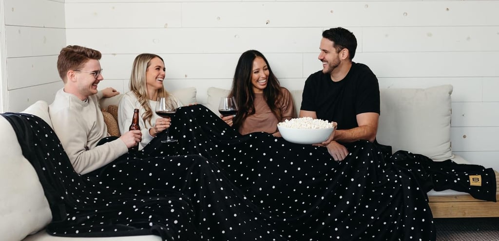 a group of 4 friends enjoying a drink together under one big extra large blanket