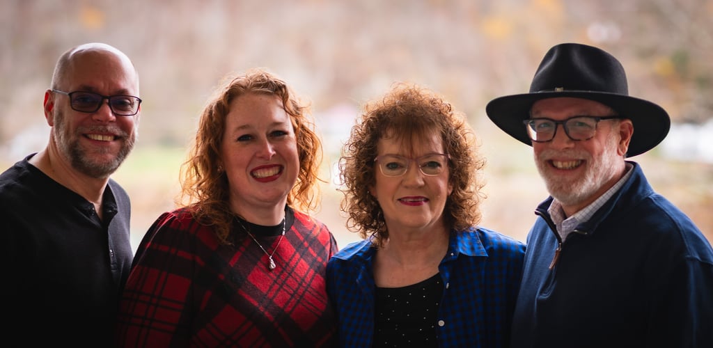 A happy group of four smiling adults posing for a family portrait outdoors during autumn.
