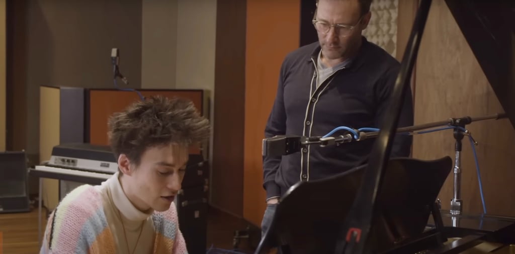 Jacob Collier sitting at the piano while Simon Sinek looks on in amazement.