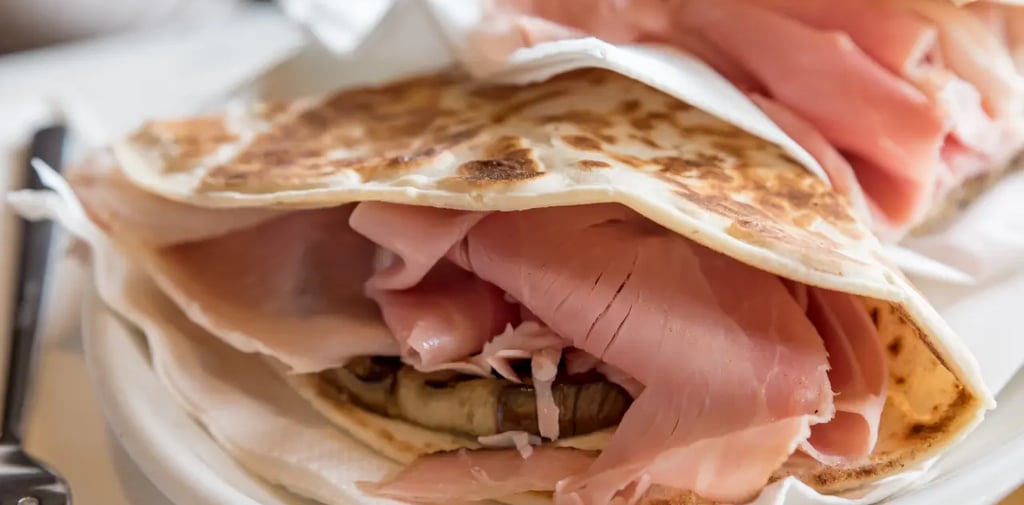 a plate of piadina romagnola with a sandwich and a fork and knife on it