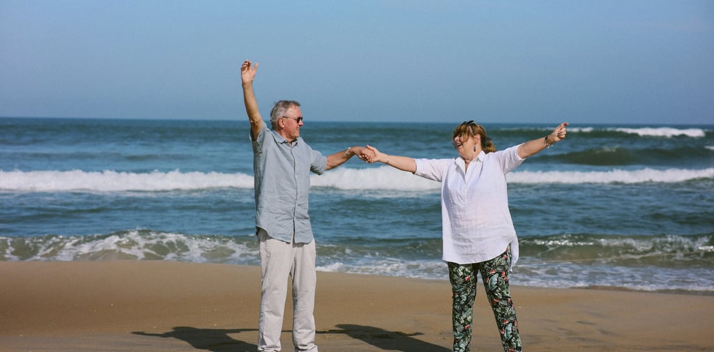 A happy senior couple holding hands and dancing on a sandy beach by the ocean waves