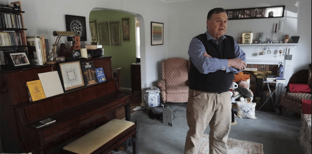 a man standing in a living room with a piano