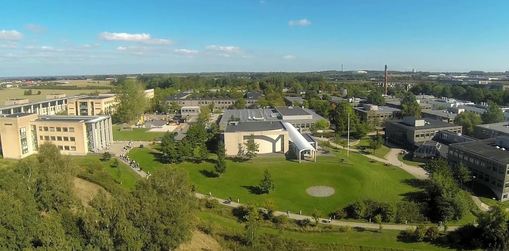 Roskilde University campus aerial view featuring a large building with a curved roof amidst green