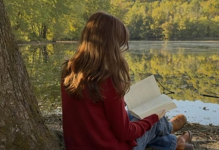 A girl reading a book on the edge of a lake