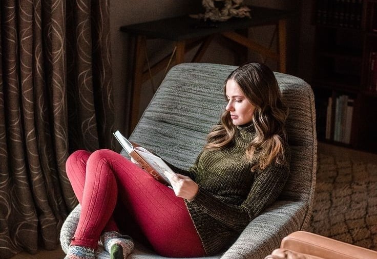 Woman sitting comfortably on a chair in her living room reading a book