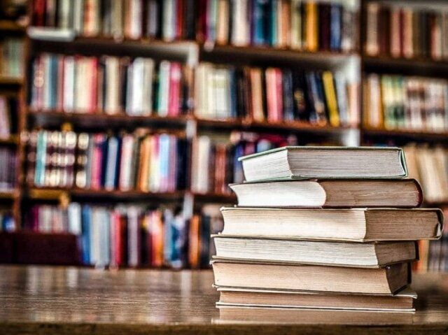 a stack of books on a table in front of a bookshelf