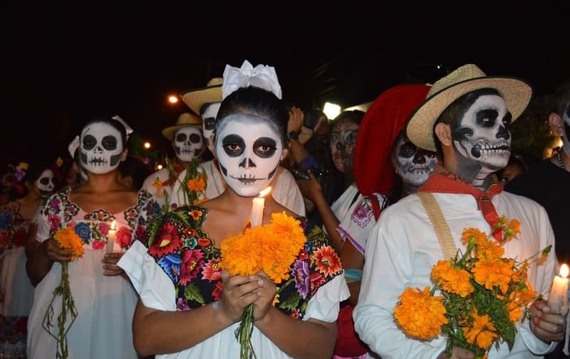 Menschen mit Totenkopf-Schminke feiern den Día de los Muertos bei Nacht mit Ringelblumen und Kerzen.