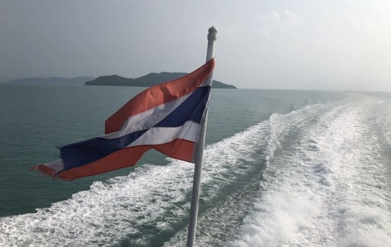 Die thailändische Flagge weht auf einem Boot auf dem Meer, mit tropischen Inseln und weißer Gischt