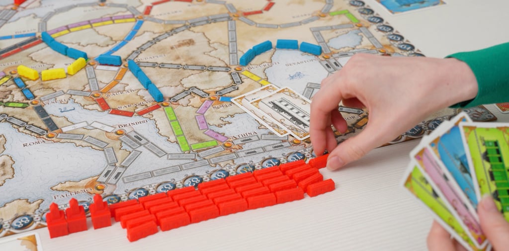 Žaidimo lenta su šalia sudėtomis vagonų figūrėlėmis, rankoje laikomos kortos