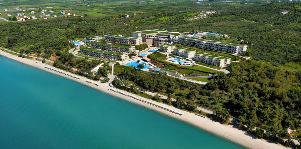 Aerial view of a luxury beachfront resort with swimming pools, turquoise sea, and lush greenery.