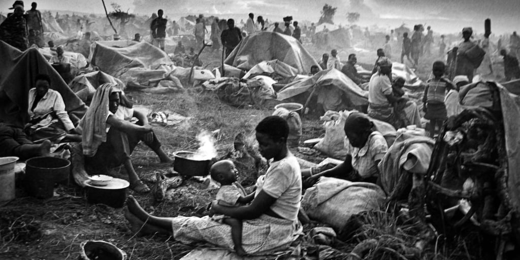A black and white photo of families in a crowded humanitarian refugee camp with makeshift tents.