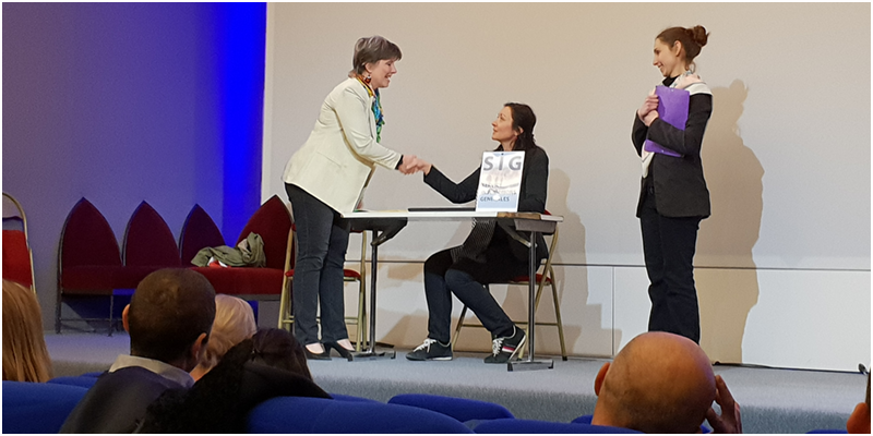 Sur scène une femme debout serre la main sous le regard d'une troisème forum accueil usager
