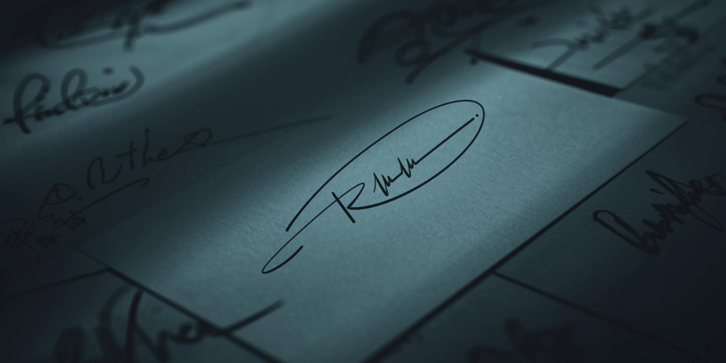 Professional handwritten signature on a business card under moody, dramatic lighting.