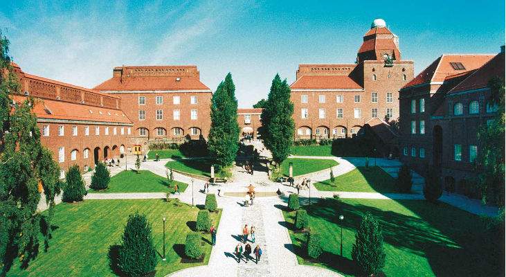 KTH Royal Institute of Technology building with red-tiled roofs, lawn, and trees under a clear blue 