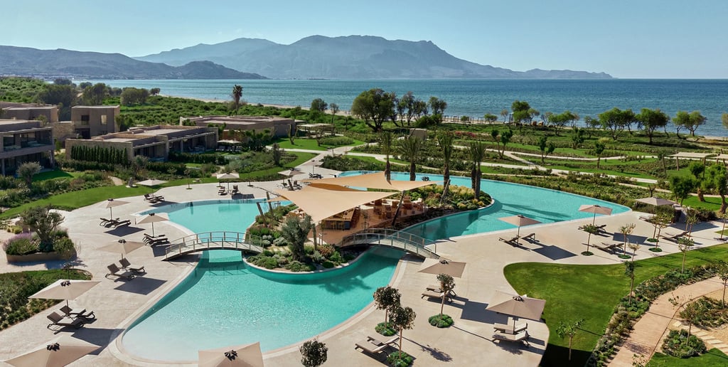 Luxury beachfront resort in Greece featuring a curved outdoor swimming pool with a pool bar and ocean views.