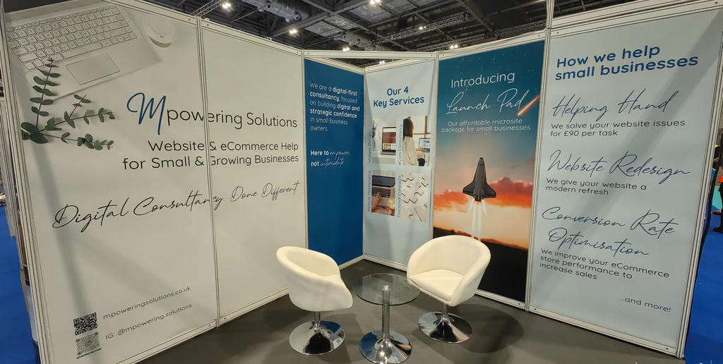 The 3x3 space Mpowering Solutions had at the Business Show in 2025, with wall panels and white furniture