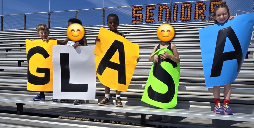 young kids holding signs that spell out GLASA and standing on bleachers