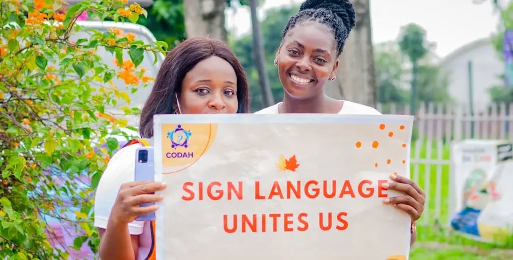 2 women smiling while holding a banner that says "Sign language unites us"