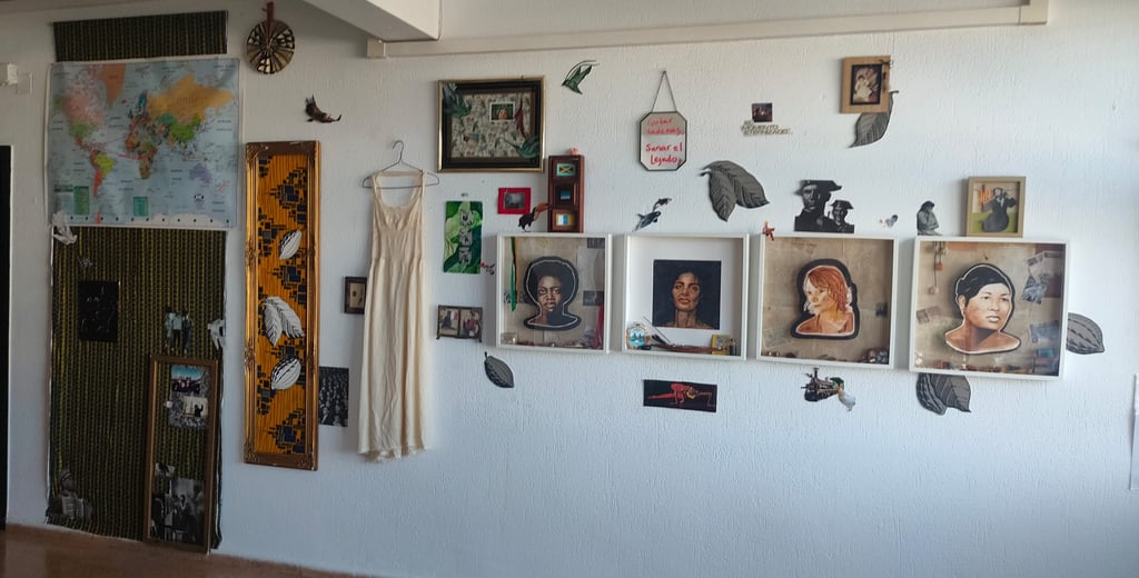 An art gallery wall featuring framed portraits, a world map, a vintage dress, and mixed media artwork.
