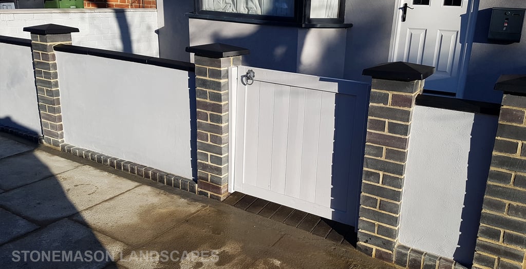 Blue perfurated brick wall with black coping and caps and grey rendering